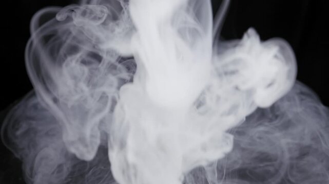White electronic cigarette with a black mouthpiece rotates as thick smoke cascades over it. Dramatic studio lighting illuminates the swirling vapor against a pitch-black background.