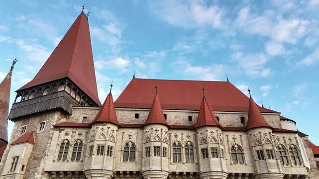 Aerial drone view of Corvin Castle in Hunedoara, Transylvania. Medieval Gothic fortress with red tiled roofs, stone towers, and dramatic defensive walls rising above the town