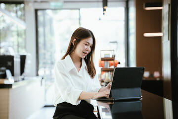 Obraz premium A young woman using a smartphone while holding a credit card, sitting at a table with a tablet in a modern cafe, representing mobile payment and online shopping lifestyle.