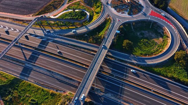 Highway interchange and traffic roundabout. High angle view of asphalt roads merging into a roundabout near agricultural fields at sunset.