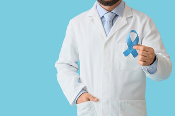 Naklejka premium Male doctor with blue ribbon on color background. Prostate cancer awareness concept