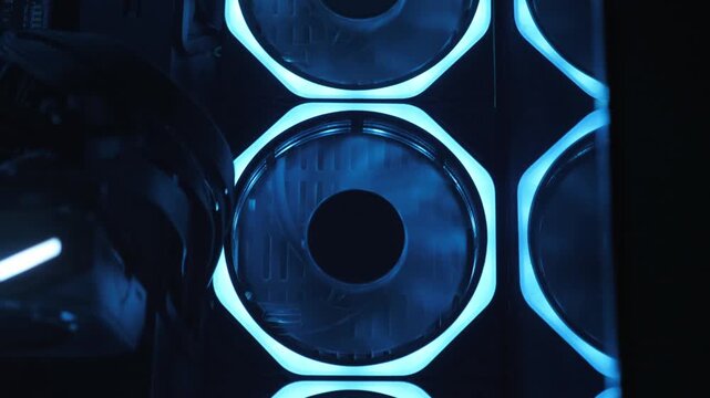 Gaming PC glowing in the dark - the system unit of a modern gaming computer. The working of the computer cooling fan can be seen through the blue lights. Fans are spinning inside the computer.