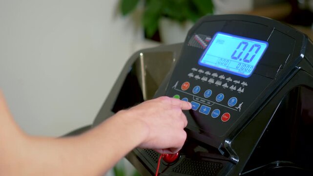Hand of unrecognizable athlete adjusting treadmill workout program on digital console before indoor cardio training. Close view of finger pressing fitness machine buttons while setting exercise