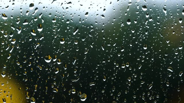 A pattern of clear aqua water droplets creates a clean liquid texture on a transparent blue glass window surface during a wet rain condensation background