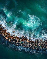 Fototapeta premium Aerial view of a wave crashing over a rocky structure in the ocean. The water is a beautiful turquoise color, and the waves create a stunning display of power and beauty. 