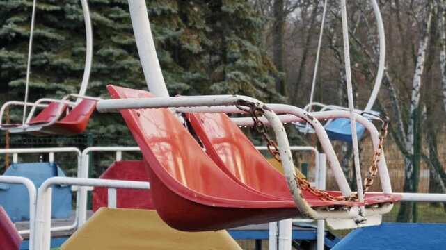 Old red swing ride sits empty in a deserted amusement park. A slow zoom-out reveals a melancholic and desolate atmosphere on an overcast day.