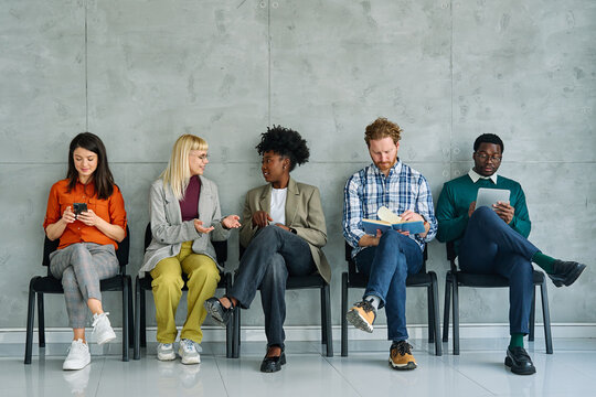 Group of young businss people sitting in chairs and waiting for an interview holding application documents