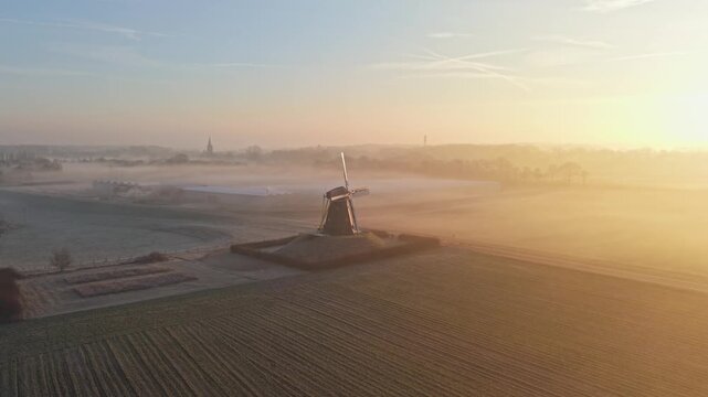 Aerial view of an old windmill standing tall amid the farmland, cloaked in ethereal mist, Beesel, Limburg, Netherlands.