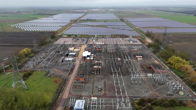 Aerial view of a vast solar farm and electrical substation under a cloudy sky, showcasing the contrast between renewable energy and power distribution, Burwell, United Kingdom.