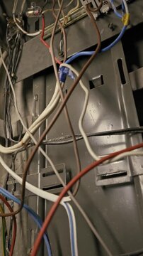 Colorful electrical wires tangle around a white terminal block inside a gray metal chassis. Camera pans slowly down the disorganized circuitry and cable connections.