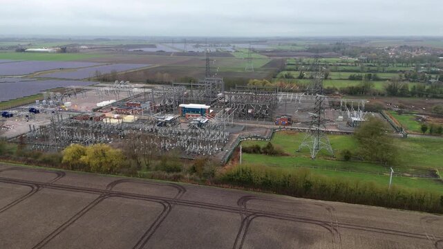 Aerial view of electrical substation with solar panels, battery energy storage systems under a cloudy sky, Burwell, United Kingdom.