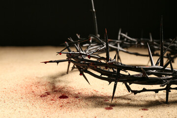 Crown of thorns with blood on sand against dark background