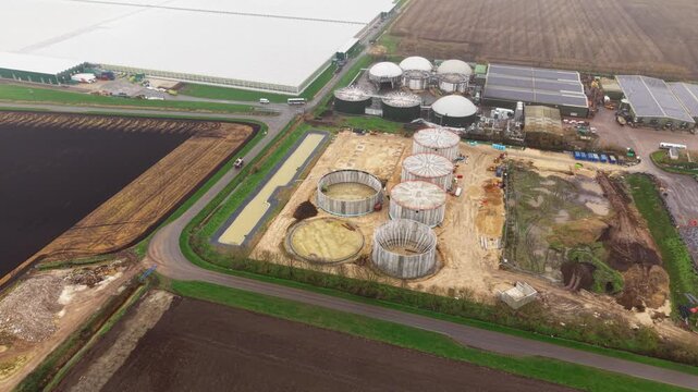Aerial view of Fenland Glasshouse Energy Centre shows a cluster of circular structures, a large greenhouse and harvested fields, Fenland, Cambridge, United Kingdom.