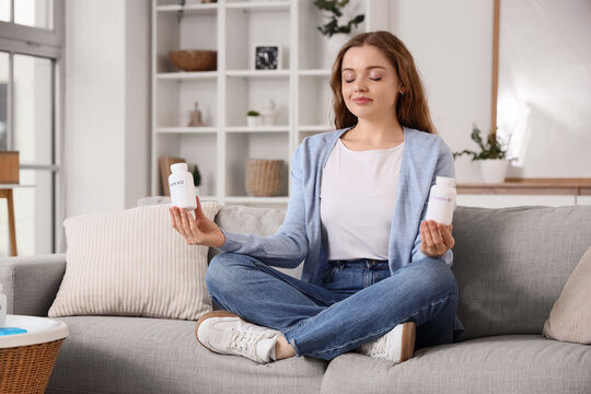 Young woman with vitamin B pills meditating on sofa at home