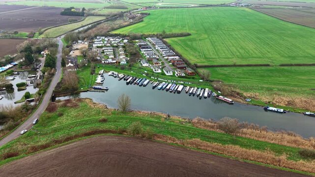 Aerial view of boats docked in Stretham Ferry Marina, a contrast of dark river water against the green fields, Stretham Ferry Marina, Ely, United Kingdom.