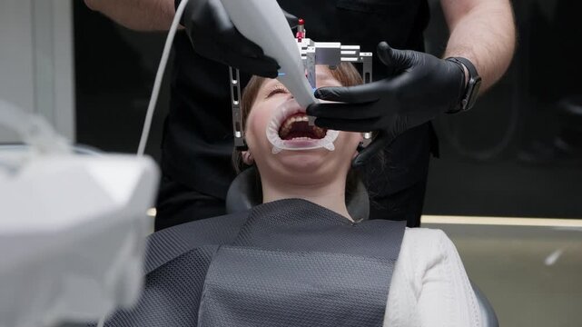 Professional orthodontist using a modern intraoral 3d scanner and dental facebow device on a female patient's teeth to create a digital model for creating dental aligners in a contemporary clinic