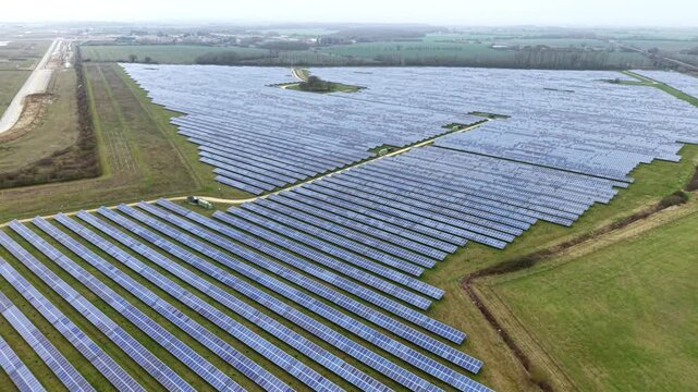 Aerial view of rows of solar panels creating a geometric pattern against the green fields, generating clean energy at former RAF Alconbury, Huntingdon, United Kingdom.