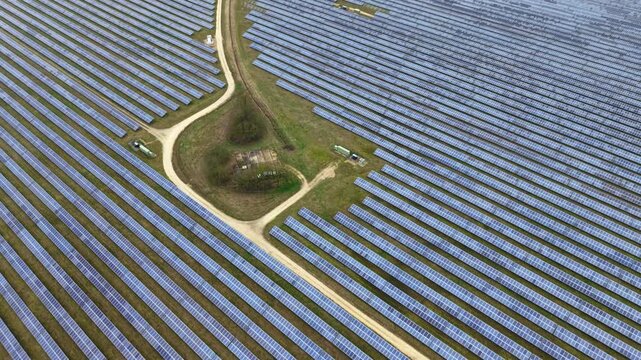Aerial view of rows of solar panels contrasted by a beige dirt road splitting the field in Former RAF Alconbury, Huntingdon, United Kingdom.