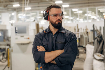 Fototapeta premium Break time, standing with arms crossed. Warehouse worker in an industrial environment of a factory or storage area