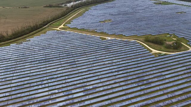 Aerial view of neatly arranged solar panels, a vast grid reflecting the sky contrasting with the surrounding greenery, Former RAF Alconbury, Huntingdon, United Kingdom.