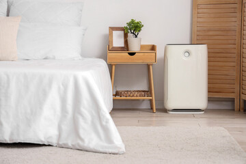 Modern air purifier near table in light bedroom