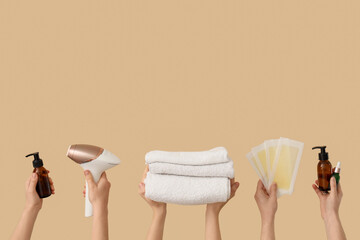 Many female hands with photoepilator, wax strips, towels and cosmetic products on beige background....