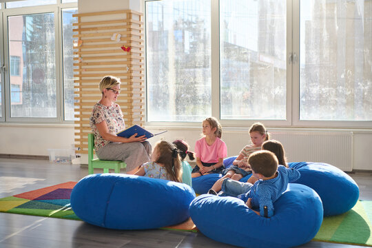 Teacher reading a picture book to young children during cozy classroom circle time on bean bags