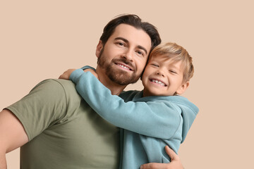 Obraz premium Smiling dad and his little son hugging on beige background. Father's day