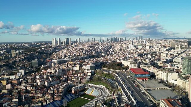Aerial view of a vibrant city with a stadium and a skyline of buildings under a blue sky with scattered clouds, Istanbul, Turkey.