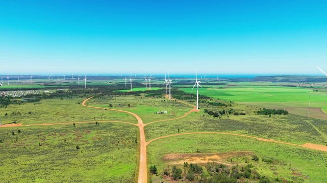 Aerial view of wind turbines standing tall amidst green fields, contrasting with the clear blue sky, Jeffreys Bay, Eastern Cape, South Africa.