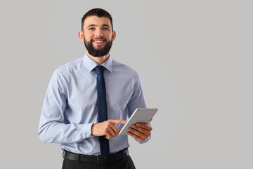 Handsome young happy businessman with tablet on grey background