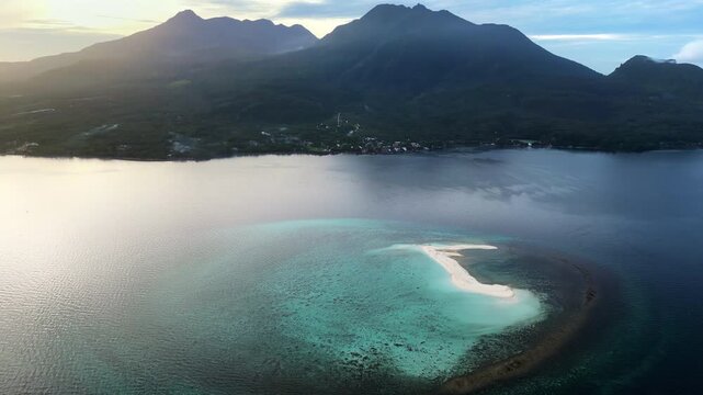 Aerial drone view of a curved sandbar in Coron Bay, Palawan, Philippines, surrounded by calm turquoise waters with dramatic mountain silhouettes in the background