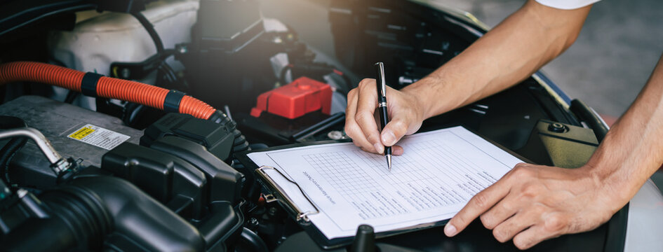 Auto check up and car service shop concept. Mechanic writing job checklist to clipboard to estimate repair quotation to client at workshop garage.