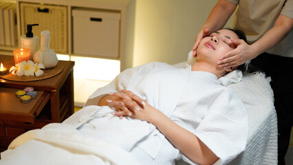 Obraz premium Young woman enjoys a calming facial treatment at a spa, with hands of a massage therapist applying soothing techniques. Skincare routine, Beauty Salon. Wellness, spa