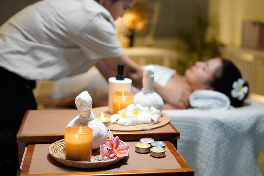 Aromatherapy massage ambiance or spa salon composition setup, focus decor candles and spa accessories and blurred woman enjoying blissful aroma spa massage in resort or hotel background