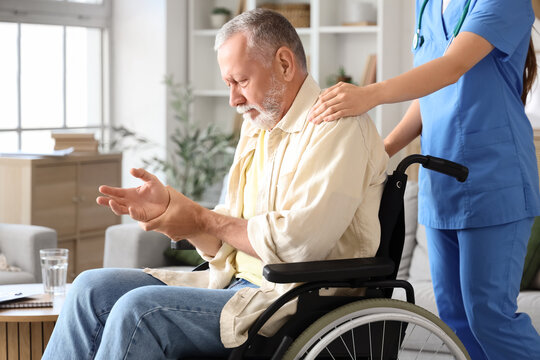 Senior man suffering from Parkinson syndrome in wheelchair with nurse at home