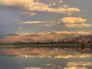 Obraz premium A scenic wide-angle landscape featuring a calm river in the foreground with a crisp mirror reflection of the surrounding environment. In the background, majestic mountains are bathed in the warm.