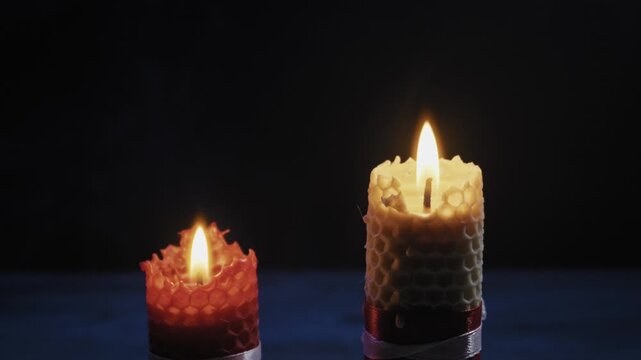 Two textured beeswax candles, one red and one yellow, burn against a dark background before being extinguished. Concept of spirituality, meditation, mourning, ritual, and the passage of time