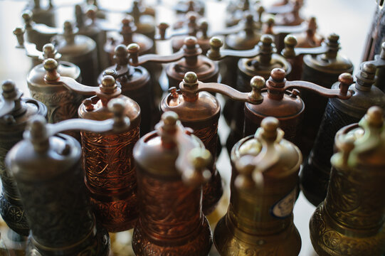A close-up horizontal shot of multiple vintage-style metal coffee or pepper mills with ornate engravings, arranged in rows on a shop shelf.