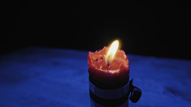 Close-up of a red candle burning in blue light before extinguishing into rising smoke. Concept of mystery, spiritual rituals, magic spells, and the end of hope or life.