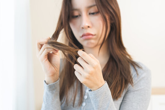 Damaged Hair, frustrated asian young woman, girl hand in holding splitting ends, messy unbrushed dry hair with face upset, long disheveled hair, health care of beauty. Portrait isolated on background