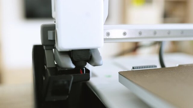 Close-up view of a 3D printer nozzle depositing molten red filament onto a build plate, showcasing the additive manufacturing process