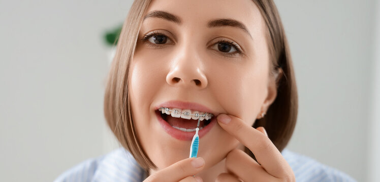 Young woman with dental braces cleaning teeth in bathroom, closeup