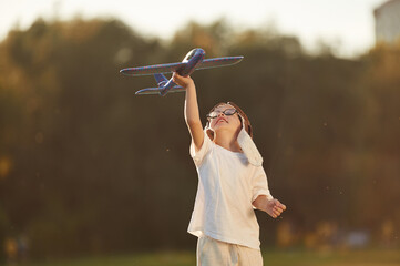 Retro style aviator hat, with toy plane. Boy is having fun on the field under sunlight at daytime © standret