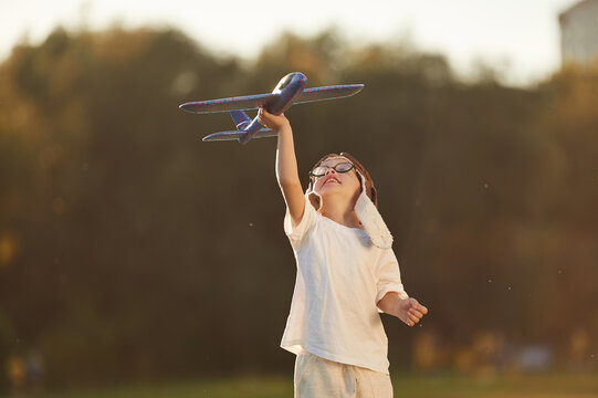 Retro style aviator hat, with toy plane. Boy is having fun on the field under sunlight at daytime