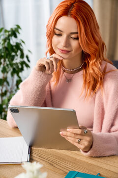 A young woman with red hair relaxes in her cozy winter clothes while using a tablet