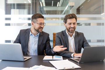 Two smiling professional businessmen are discussing work and collaborating on a project, reviewing...