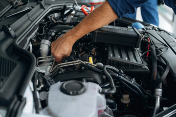 Fixing the car, hood is opened. Close up view of male service station worker at job