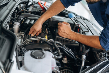 Obraz premium Hands visible only, hood is opened, fixing. Close up view of male service station worker at job