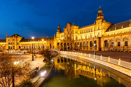 Travel, tourism: Plaza de Espa&ntilde;a illuminated at night, reflecting in the water, showcasing Spanish architecture and culture in Seville, Spain.